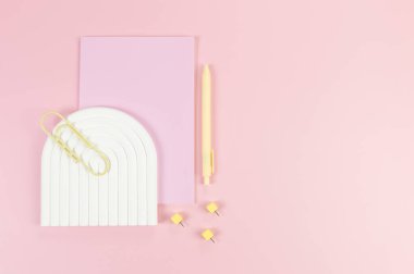Pembe defterin üst görüntüsü, sarı kalem, ataç, raptiyeler, pembe arka planda beyaz kemer tepsisi. Okul, ofis duvar kağıdı. Düz yat, boşluğu kopyala.