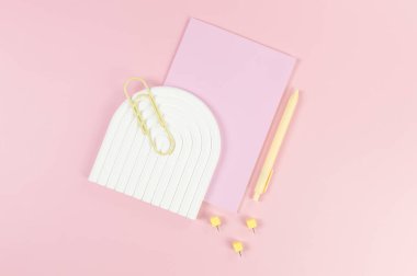 Pembe defterin üst görüntüsü, sarı kalem, ataç, raptiyeler, pembe arka planda beyaz kemer tepsisi. Okul, ofis duvar kağıdı. Düz yat, boşluğu kopyala.