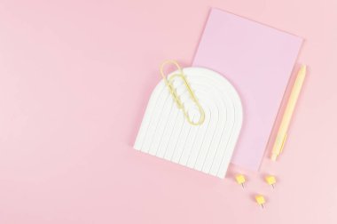 Pembe defterin üst görüntüsü, sarı kalem, ataç, raptiyeler, pembe arka planda beyaz kemer tepsisi. Okul, ofis duvar kağıdı. Düz yat, boşluğu kopyala.