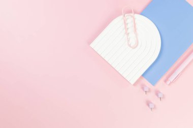Mavi defterin üst görüntüsü, pembe kalem, ataç, raptiyeler, pembe arka planda beyaz kemer tepsisi. Okul, ofis duvar kağıdı. Düz yat, boşluğu kopyala.