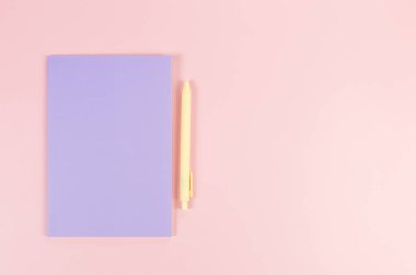 Mor defterin üst görüntüsü, pembe arka planda sarı kalem. Okul, ofis duvar kağıdı. Düz yat, boşluğu kopyala.
