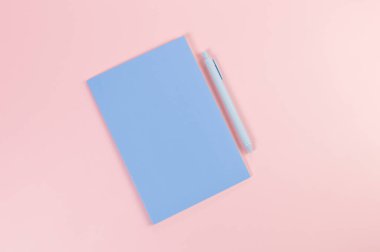 Mavi defterin üst görüntüsü, pembe arka planda mavi kalem. Okul, ofis duvar kağıdı. Düz yat, boşluğu kopyala.