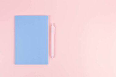 Mavi defterin üst görüntüsü, pembe arka planda pembe kalem. Okul, ofis duvar kağıdı. Düz yat, boşluğu kopyala.