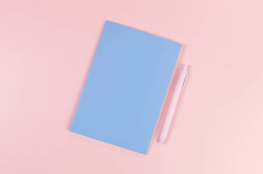 Mavi defterin üst görüntüsü, pembe arka planda pembe kalem. Okul, ofis duvar kağıdı. Düz yat, boşluğu kopyala.