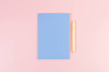 Mavi defterin üst görüntüsü, pembe arka planda sarı kalem. Okul, ofis duvar kağıdı. Düz yat, boşluğu kopyala.
