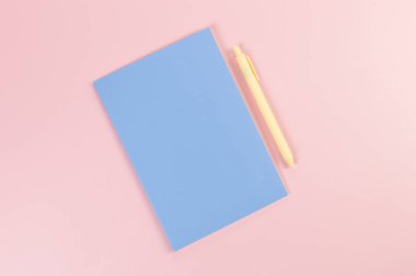 Mavi defterin üst görüntüsü, pembe arka planda sarı kalem. Okul, ofis duvar kağıdı. Düz yat, boşluğu kopyala.