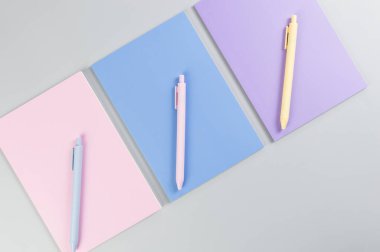 Gri arkaplanda pembe, mor ve mavi defterlerin üst görüntüsü. Pembe, sarı ve mavi kalemler, okul, ofis kağıdı. Düz yat, boşluğu kopyala.