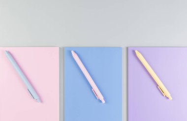 Gri arkaplanda pembe, mor ve mavi defterlerin üst görüntüsü. Pembe, sarı ve mavi kalemler, okul, ofis kağıdı. Düz yat, boşluğu kopyala.