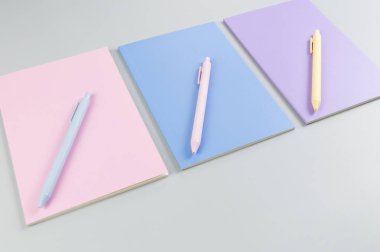 Gri arkaplanda pembe, mor ve mavi defterlerin üst görüntüsü. Pembe, sarı ve mavi kalemler, okul, ofis kağıdı. Düz yat, boşluğu kopyala.