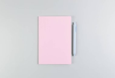 Pembe defterin üst görüntüsü, gri arka planda mavi kalem. Okul, ofis duvar kağıdı. Düz yat, boşluğu kopyala.