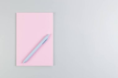 Pembe defterin üst görüntüsü, gri arka planda mavi kalem. Okul, ofis duvar kağıdı. Düz yat, boşluğu kopyala.