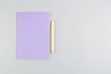 Mor defterin üst görüntüsü, gri arkaplanda sarı kalem. Okul, ofis duvar kağıdı. Düz yat, boşluğu kopyala.