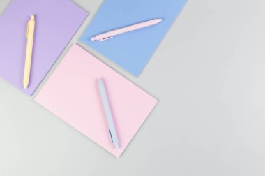 Gri arkaplanda pembe, mor ve mavi defterlerin üst görüntüsü. Pembe, sarı ve mavi kalemler, okul, ofis kağıdı. Düz yat, boşluğu kopyala.