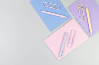 Gri arkaplanda pembe, mor ve mavi defterlerin üst görüntüsü. Pembe, sarı ve mavi kalemler, ataçlar, okul, ofis kağıdı. Düz yat, boşluğu kopyala.