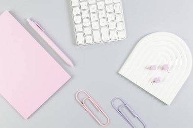 Beyaz klavyenin üst görüntüsü, pembe defter, gri arka planda pembe kalem. Raptiyeler, raptiyeler, modern ofis, okul. Beyaz kemer tepsisi, düz konum, kopyalama alanı.