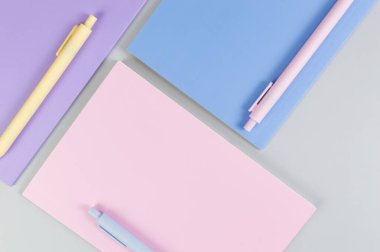 Gri arkaplanda pembe, mor ve mavi defterlerin üst görüntüsü. Pembe, sarı ve mavi kalemler, okul, ofis kağıdı. Düz yat, boşluğu kopyala.