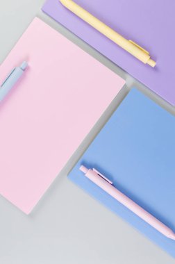 Gri arkaplanda pembe, mor ve mavi defterlerin üst görüntüsü. Pembe, sarı ve mavi kalemler, okul, ofis kağıdı. Düz yat, boşluğu kopyala.