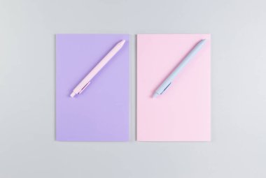 Pembe ve mor defterlerin üst görüntüsü, gri arka planda pembe ve mavi kalemler. Okul, ofis duvar kağıdı. Düz yat, boşluğu kopyala.