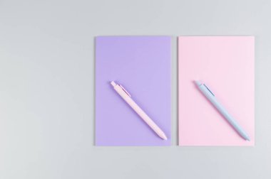 Pembe ve mor defterlerin üst görüntüsü, gri arka planda pembe ve mavi kalemler. Okul, ofis duvar kağıdı. Düz yat, boşluğu kopyala.