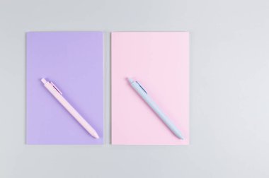 Pembe ve mor defterlerin üst görüntüsü, gri arka planda pembe ve mavi kalemler. Okul, ofis duvar kağıdı. Düz yat, boşluğu kopyala.