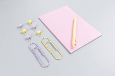 Gri arkaplandaki pembe defterin üst görüntüsü. Ataç, kalem ve raptiye. Okul, ofis duvar kağıdı. Düz yat, boşluğu kopyala.