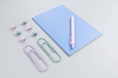 Gri arkaplanda mavi defterin üst görüntüsü. Ataç, kalem ve raptiye. Okul, ofis duvar kağıdı. Düz yat, boşluğu kopyala.