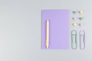 Gri arkaplandaki mor defterin üst görüntüsü. Ataç, kalem ve raptiye. Okul, ofis duvar kağıdı. Düz yat, boşluğu kopyala.