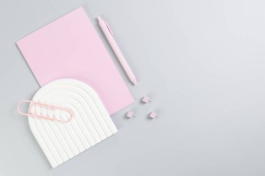 Pembe defter, pembe kalem, ataç, raptiyeler, gri arka planda beyaz kemer tepsisi. Okul, ofis duvar kağıdı. Düz yat, boşluğu kopyala.