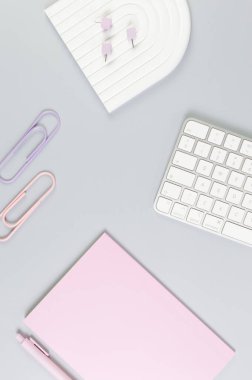Beyaz klavyenin üst görüntüsü, pembe defter, gri arka planda pembe kalem. Raptiyeler, raptiyeler, modern ofis, okul. Beyaz kemer tepsisi, düz konum, kopyalama alanı.