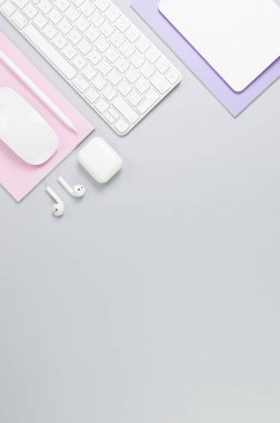 Beyaz klavye, fare, dokunmatik ped, kulaklık kutusu, gri arka planda kalem. Mor ve pembe defterler, modern ofis, okul. Düz yat, boşluğu kopyala.