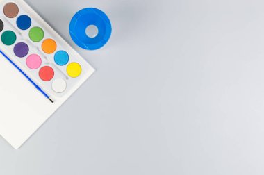 Suluboya, kağıt, su kabı ve gri arka planda boya fırçası. Resim, sanat, kopyalama alanı, düzlük.