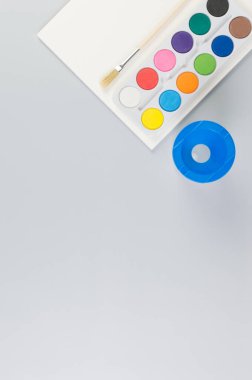 Suluboya, boya fırçası, kağıt ve su kabının üst görüntüsü gri arka planda. Resim, sanat, kopyalama alanı, düzlük.