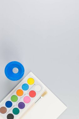 Suluboya, boya fırçası, kağıt ve su kabının üst görüntüsü gri arka planda. Resim, sanat, kopyalama alanı, düzlük.