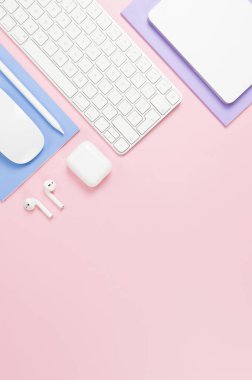 Beyaz klavye, fare, dokunmatik ped, kulaklık kutusu, pembe arka planda kalem. Mor ve mavi defterler, modern ofis, okul. Düz yat, boşluğu kopyala.