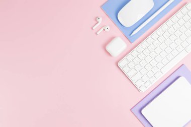 Beyaz klavye, fare, dokunmatik ped, kulaklık kutusu, pembe arka planda kalem. Mor ve mavi defterler, modern ofis, okul. Düz yat, boşluğu kopyala.