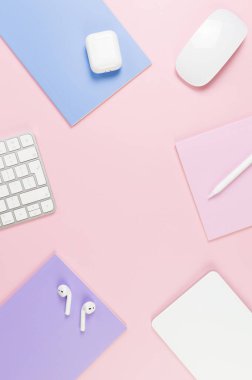 Beyaz klavye, fare, dokunmatik ped, kulaklık kutusu, pembe arka planda kalem. Mor, pembe ve mavi defterler, modern ofis, okul. Düz yat, boşluğu kopyala.