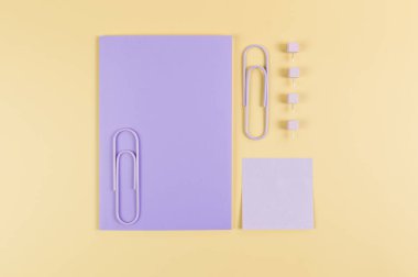 Sarı arkaplanda mor defterin üst görüntüsü. Mor yapışkan not, ataç ve raptiyeler. Okul, ofis duvar kağıdı. Düz yat, boşluğu kopyala.