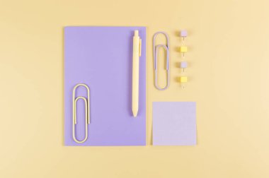 Sarı arkaplanda mor defterin üst görüntüsü. Yapışkan not, ataç, kalem ve iğne. Okul, ofis duvar kağıdı. Düz yat, boşluğu kopyala.