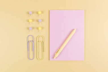 Sarı arkaplanda pembe defterin üst görüntüsü. Ataç, kalem ve raptiye. Okul, ofis duvar kağıdı. Düz yat, boşluğu kopyala.