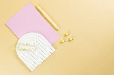 Pembe defterin üst görüntüsü, sarı kalem, ataç, raptiyeler, sarı arka planda beyaz kemer tepsisi. Okul, ofis duvar kağıdı. Düz yat, boşluğu kopyala.
