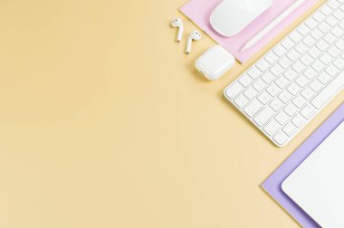 Beyaz klavye, fare, dokunmatik ped, kulaklık kutusu, sarı arka planda kalem. Mor ve pembe defterler, modern ofis, okul. Düz yat, boşluğu kopyala.