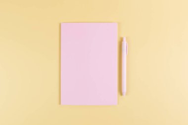 Pembe defterin üst görüntüsü, sarı arka planda pembe kalem. Okul, ofis duvar kağıdı. Düz yat, boşluğu kopyala.