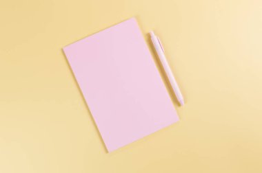 Pembe defterin üst görüntüsü, sarı arka planda pembe kalem. Okul, ofis duvar kağıdı. Düz yat, boşluğu kopyala.