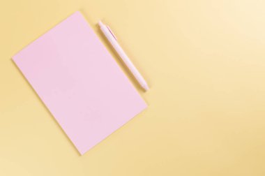 Pembe defterin üst görüntüsü, sarı arka planda pembe kalem. Okul, ofis duvar kağıdı. Düz yat, boşluğu kopyala.
