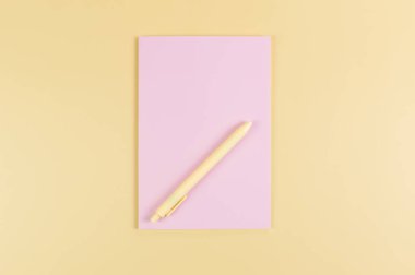 Pembe defterin üst görüntüsü, sarı arka planda sarı kalem. Okul, ofis duvar kağıdı. Düz yat, boşluğu kopyala.