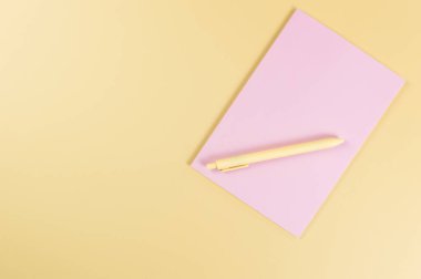 Pembe defterin üst görüntüsü, sarı arka planda sarı kalem. Okul, ofis duvar kağıdı. Düz yat, boşluğu kopyala.