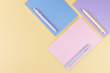 Sarı arka planda pembe, mor ve mavi defterlerin üst görüntüsü. Pembe, sarı ve mavi kalemler, okul, ofis kağıdı. Düz yat, boşluğu kopyala.