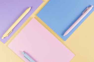 Sarı arka planda pembe, mor ve mavi defterlerin üst görüntüsü. Pembe, sarı ve mavi kalemler, okul, ofis kağıdı. Düz yat, boşluğu kopyala.