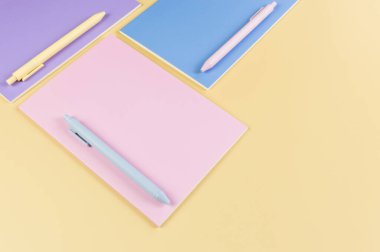 Sarı arka planda pembe, mor ve mavi defterlerin üst görüntüsü. Pembe, sarı ve mavi kalemler, okul, ofis kağıdı. Düz yat, boşluğu kopyala.