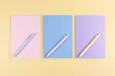 Sarı arka planda pembe, mor ve mavi defterlerin üst görüntüsü. Pembe, sarı ve mavi kalemler, okul, ofis kağıdı. Düz yat, boşluğu kopyala.